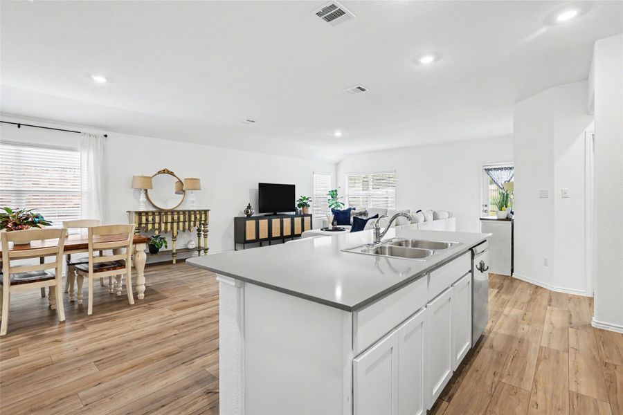 Open-concept living area featuring wood-finish flooring, recessed lighting, and a kitchen island with a double basin sink and light-toned countertop