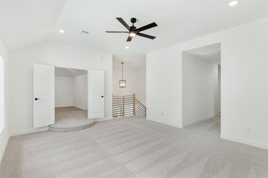 Spacious upstairs bonus room with carpet, ceiling fan, vaulted ceiling, and open staircase railing nearby. Spacious upstairs bonus room with carpet, ceiling fan, vaulted ceiling, and open staircase railing nearby.