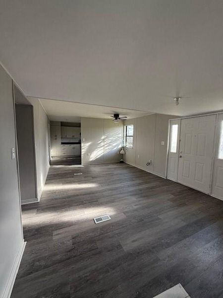 Expansive open-concept living area featuring wood-finish flooring, light gray wall panels, and a ceiling fan