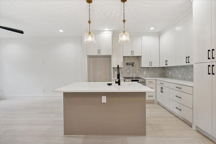 Kitchen featuring decorative backsplash, white cabinets, a kitchen island with sink, and pendant lighting