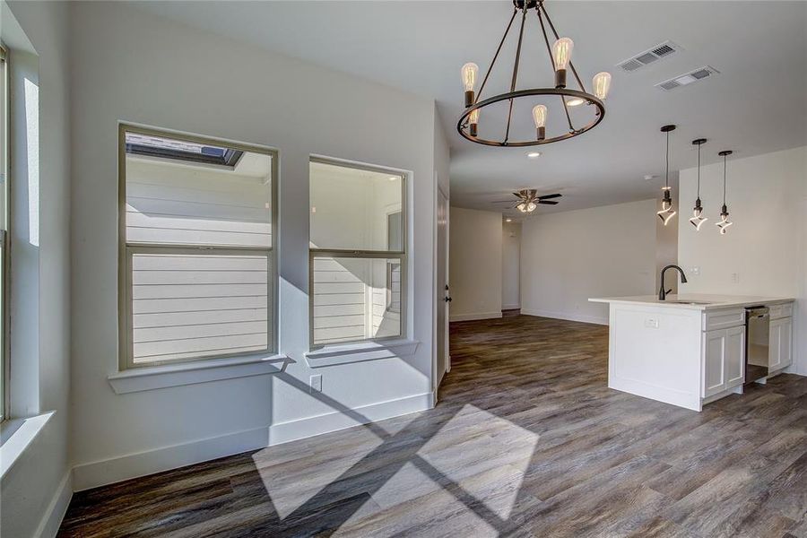 Kitchen featuring pendant lighting, a chandelier, open floor plan, light stone countertops, and stainless steel dishwasher Kitchen featuring pendant lighting, a chandelier, open floor plan, light stone countertops, and stainless steel dishwasher