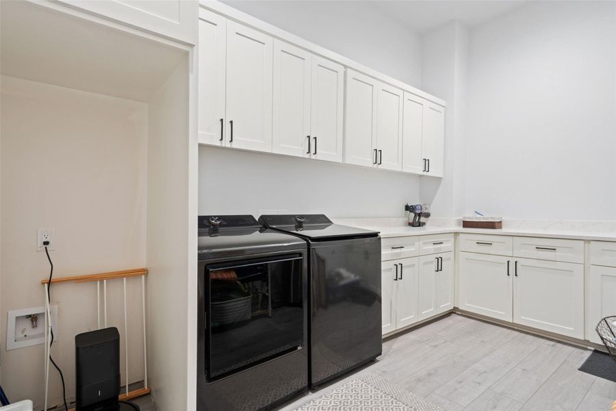 White shaker cabinetry with matte black hardware, light-toned wood-finish flooring, and white countertops