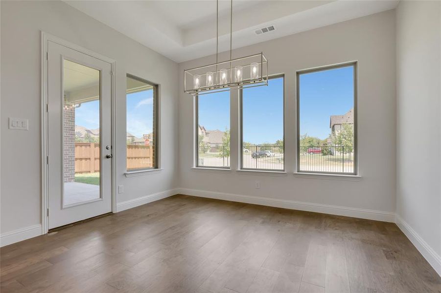 Unfurnished dining area with a raised ceiling, hardwood / wood-style flooring, and a chandelier