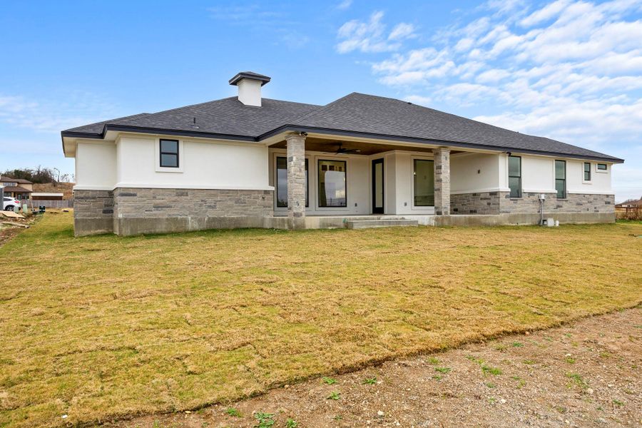Rear view of house with a yard, a patio area, stucco siding, and stone siding