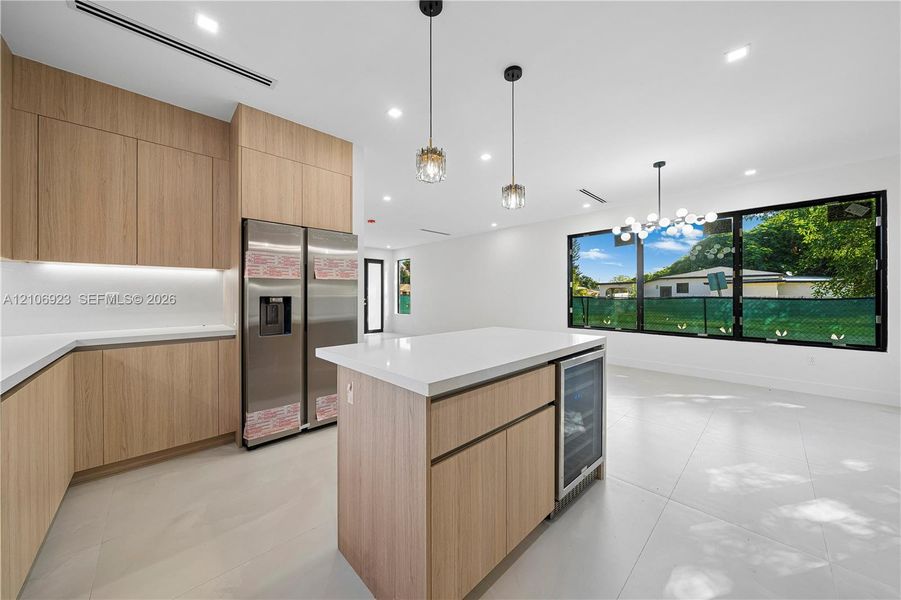 Kitchen featuring wood-finish flat-panel cabinetry, quartz countertops, a central island with an integrated wine cooler, stainless steel refrigerator, and large picture windows Kitchen featuring wood-finish flat-panel cabinetry, quartz countertops, a central island with an integrated wine cooler, stainless steel refrigerator, and large picture windows