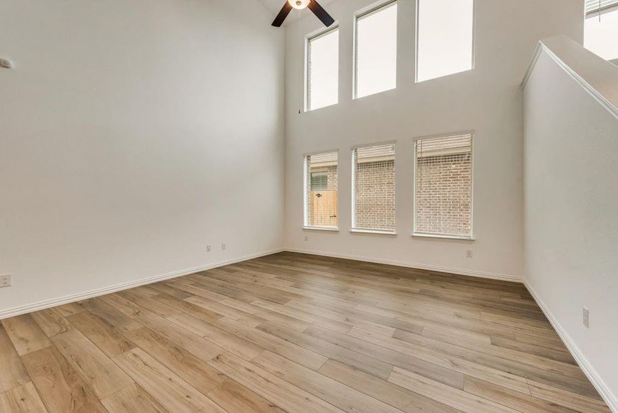 Unfurnished living room featuring a towering ceiling, ceiling fan, and light hardwood / wood-style floors