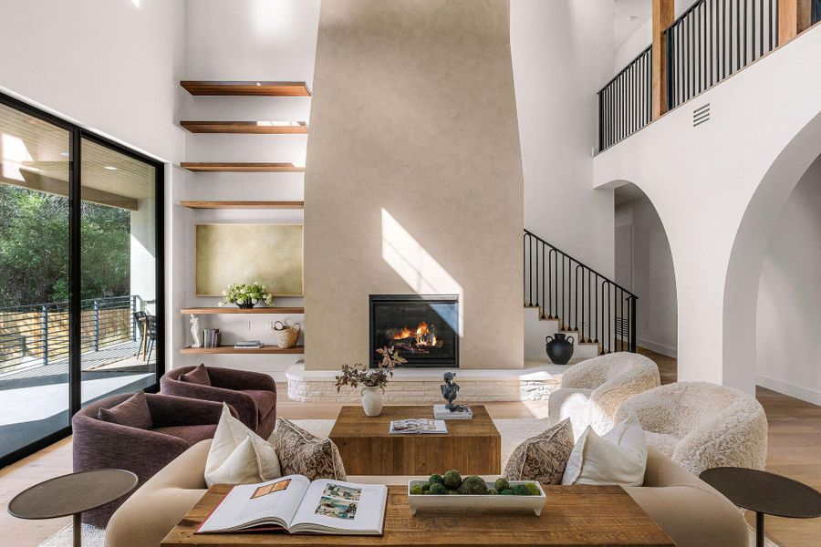 A grand living space with towering ceilings and a striking fireplace opens to a serene outdoor patio.