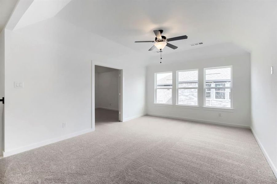 Spacious room featuring vaulted ceilings, light-hued carpeting, and a trio of windows providing ambient light Spacious room featuring vaulted ceilings, light-hued carpeting, and a trio of windows providing ambient light