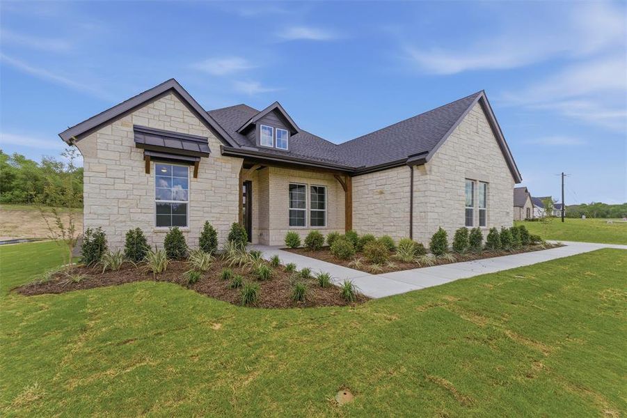 View of front facade with stone siding, covered porch, a front yard, and roof with shingles