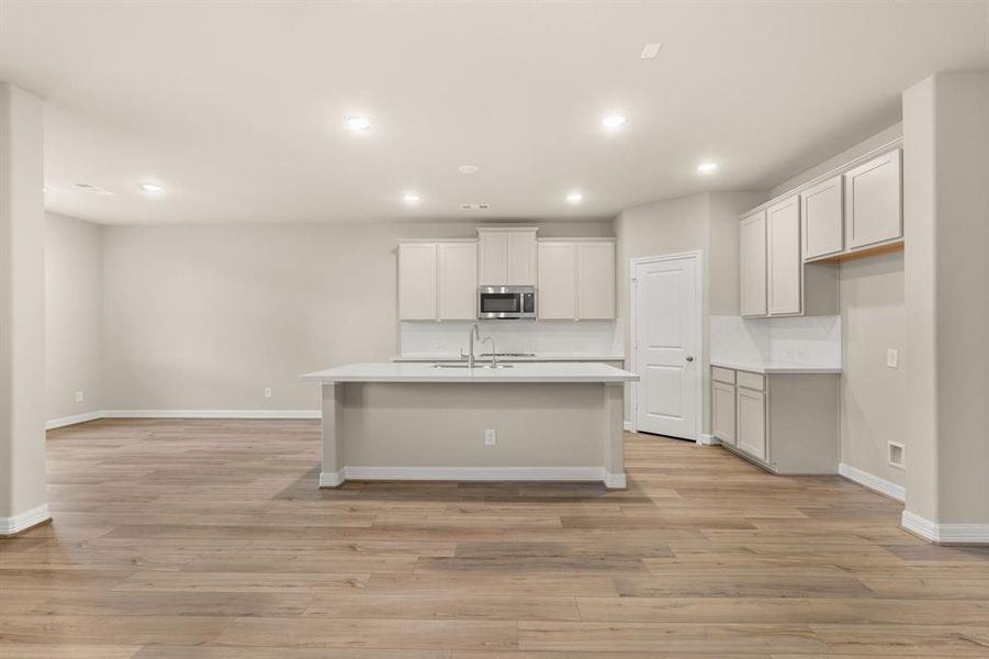 This light and bright kitchen features a large quartz island, white cabinets, a large sink overlooking your family room, recessed lighting, and beautiful backsplash.