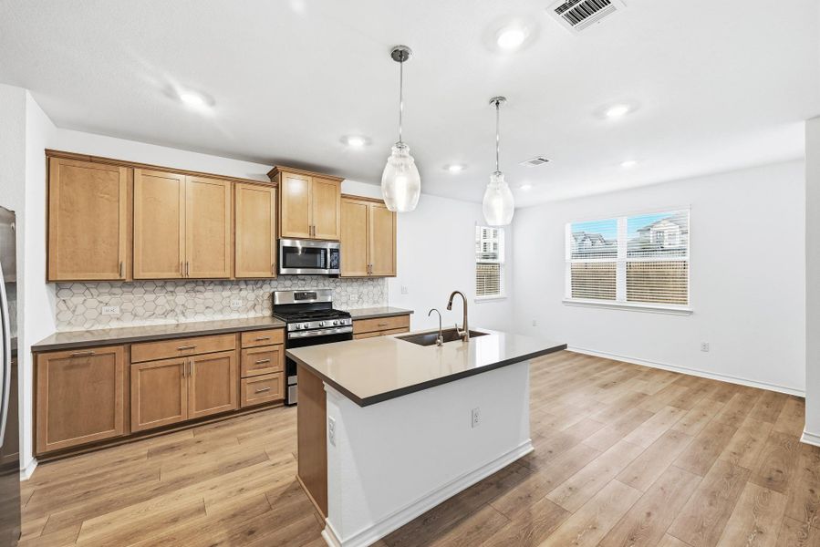 Kitchen featuring stainless steel appliances, backsplash, a center island with sink, pendant lighting, and light wood-style flooring