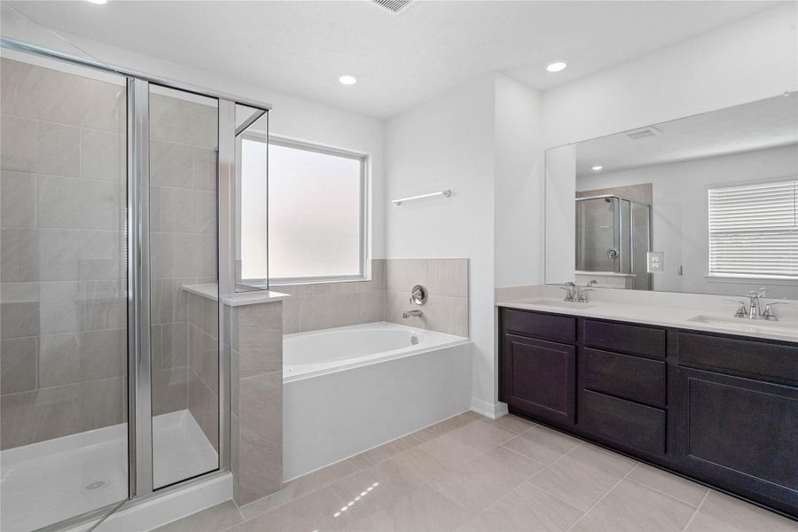 This primary bathroom is definitely move-in ready! Featuring dual sinks, stained cabinets with light countertops, mirror, high ceilings, neutral paint, soaking tub, walk-in shower with tile surround, dark sleek fixtures, and modern finishes.