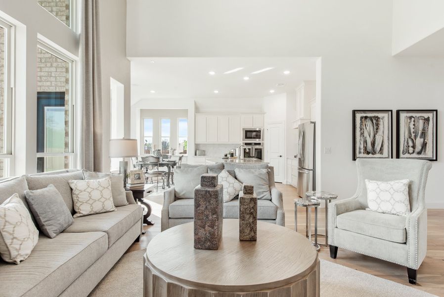 Open-concept living room with gray sofas, high ceilings, and kitchen visible in background Open-concept living room with gray sofas, high ceilings, and kitchen visible in background