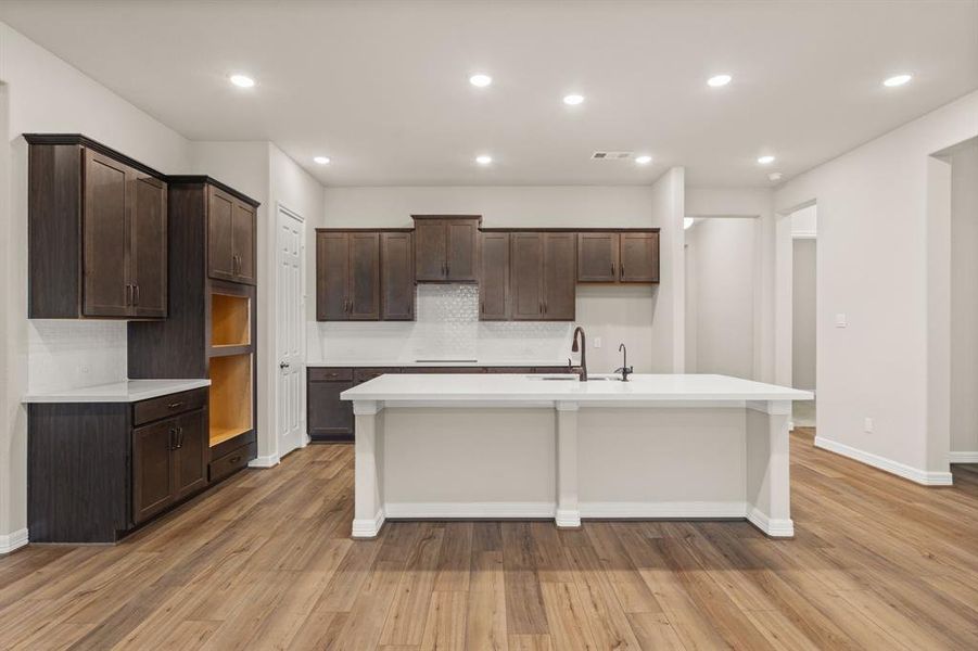 This light and bright kitchen features a large quartz island, dark stained cabinets, a large sink overlooking your family room, recessed lighting, and beautiful backsplash.