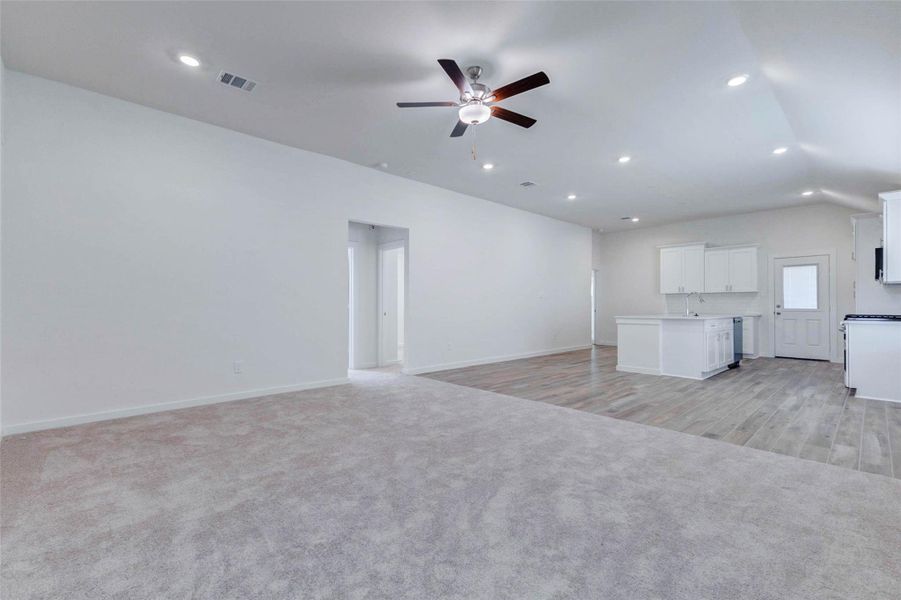 Spacious open-concept living area with high ceilings, recessed lighting, ceiling fan, soft carpet in the family room, and wood-look tile flowing into the kitchen and dining space. The layout feels bright, airy, and connected, ideal for everyday living and entertaining.