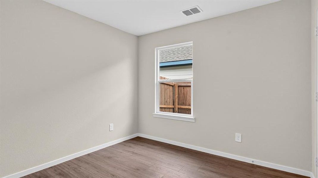 Neutral wall finishes and rich wood-finish flooring define this bright interior space, featuring a single window with white trim, crisp white baseboards, and a ceiling vent