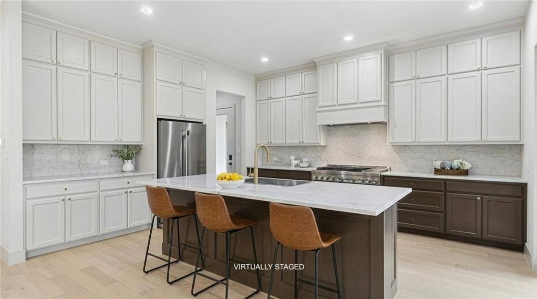 Gourmet kitchen featuring a central island with white countertop, extensive white cabinetry, professional-grade range, stainless steel refrigerator, and white oak pre engineered wood flooring. Extended cabinetry and upgraded stone countertops are just a few of the designer touches. Gourmet kitchen featuring a central island with white countertop, extensive white cabinetry, professional-grade range, stainless steel refrigerator, and white oak pre engineered wood flooring. Extended cabinetry and upgraded stone countertops are just a few of the designer touches.
