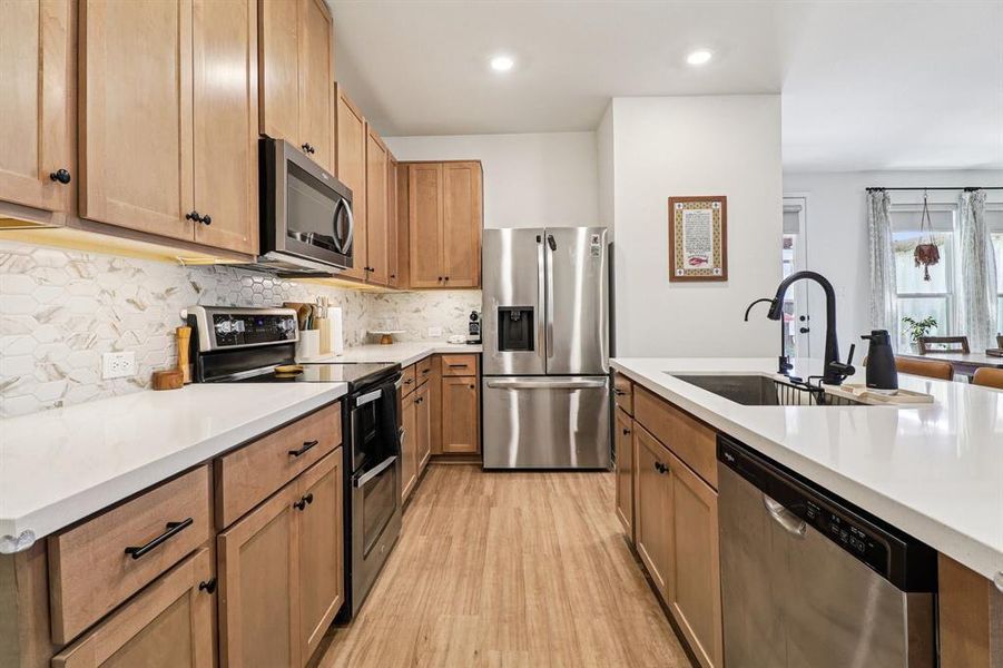 Kitchen featuring stainless steel appliances, tasteful backsplash, light wood finished floors, recessed lighting, and light stone counters Kitchen featuring stainless steel appliances, tasteful backsplash, light wood finished floors, recessed lighting, and light stone counters
