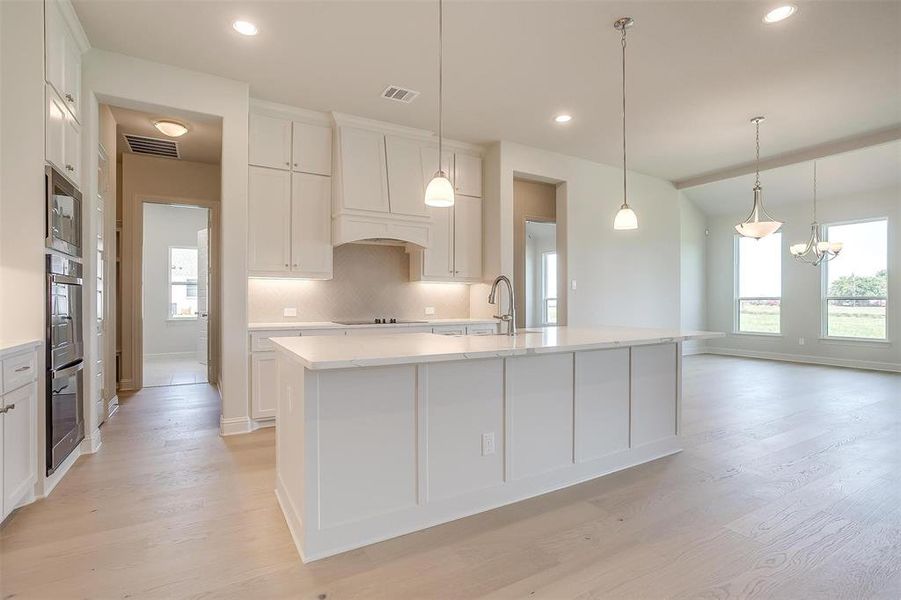 Kitchen with light hardwood / wood-style floors, a kitchen island with sink, tasteful backsplash, stainless steel appliances, and white cabinets