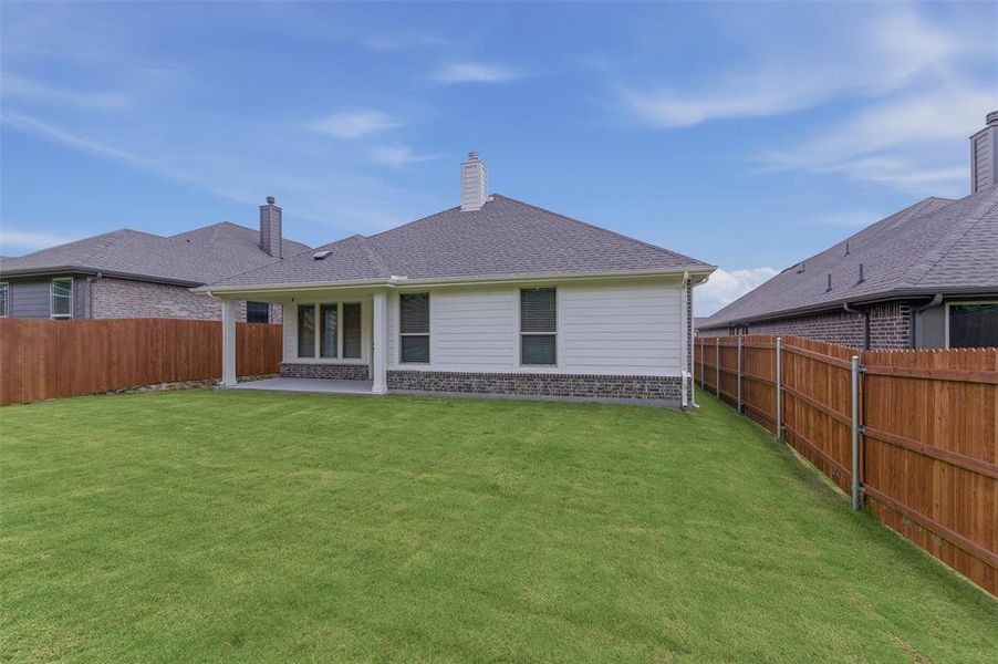 Expansive backyard featuring a manicured lawn, full wood fencing, and a covered concrete patio