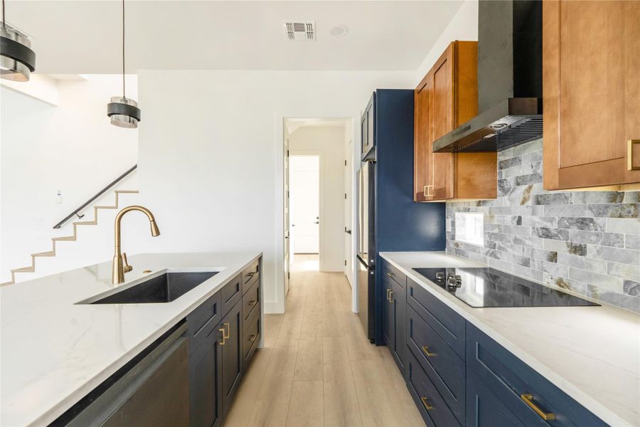Kitchen with light stone countertops, light wood finished floors, stainless steel dishwasher, and black electric cooktop