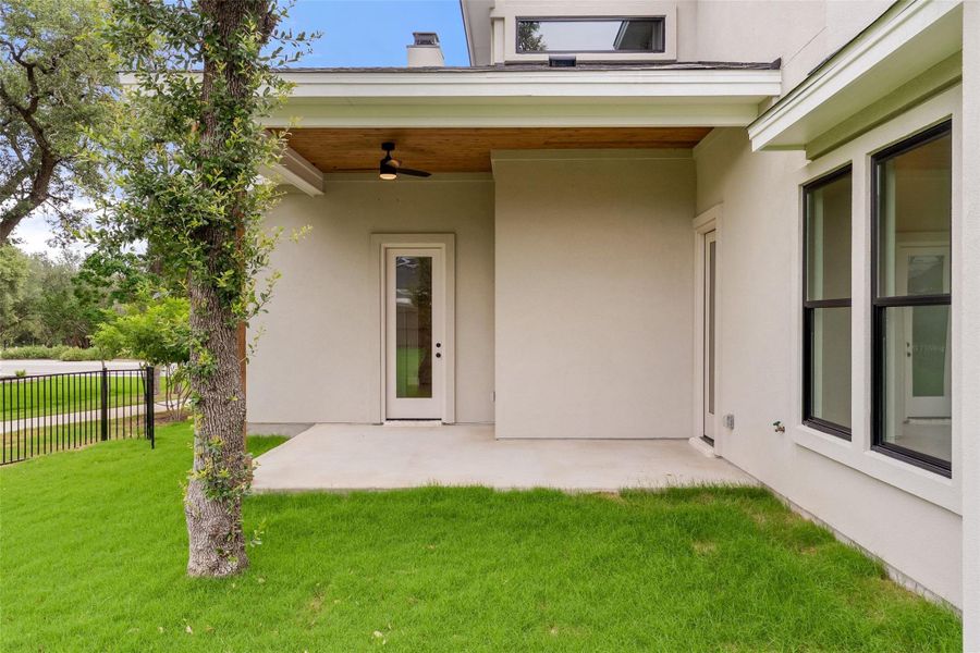 A tranquil outdoor living space features a covered patio with a modern fan and an adjacent grassy area.