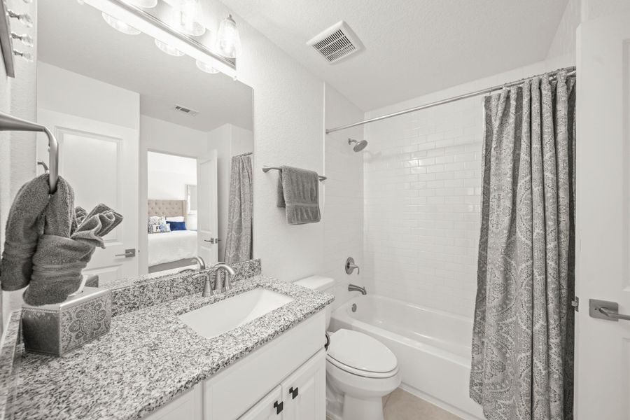 This ensuite bath features a granite counter and a tub/shower combo with subway tile extending to the ceiling.