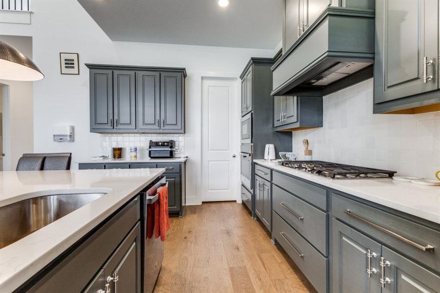 Kitchen with light wood-type flooring, light stone countertops, tasteful backsplash, and gray cabinets