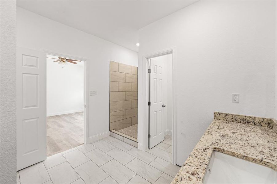 Bathroom with tile patterned floors, ceiling fan, a tile shower, and vanity