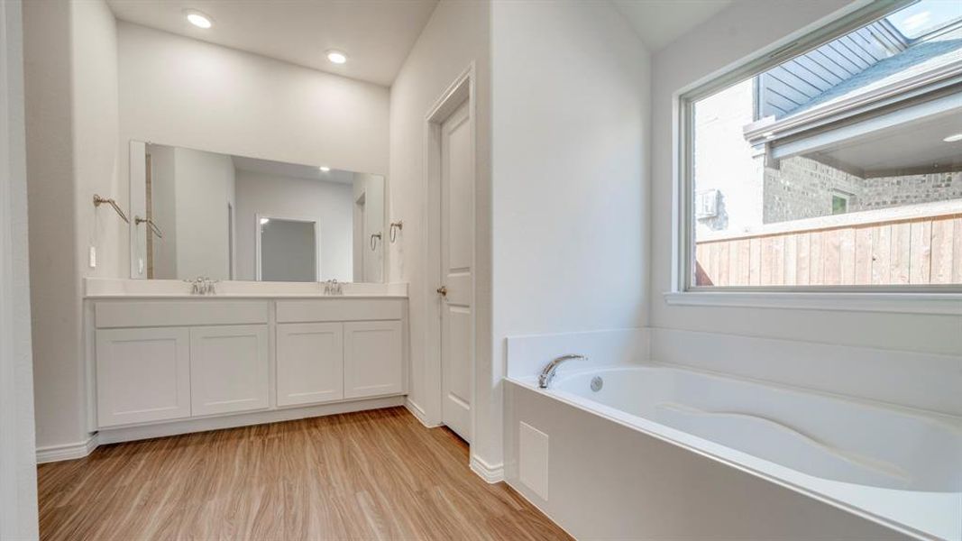 Full bathroom with double vanity, light wood finished floors, a garden tub, and recessed lighting