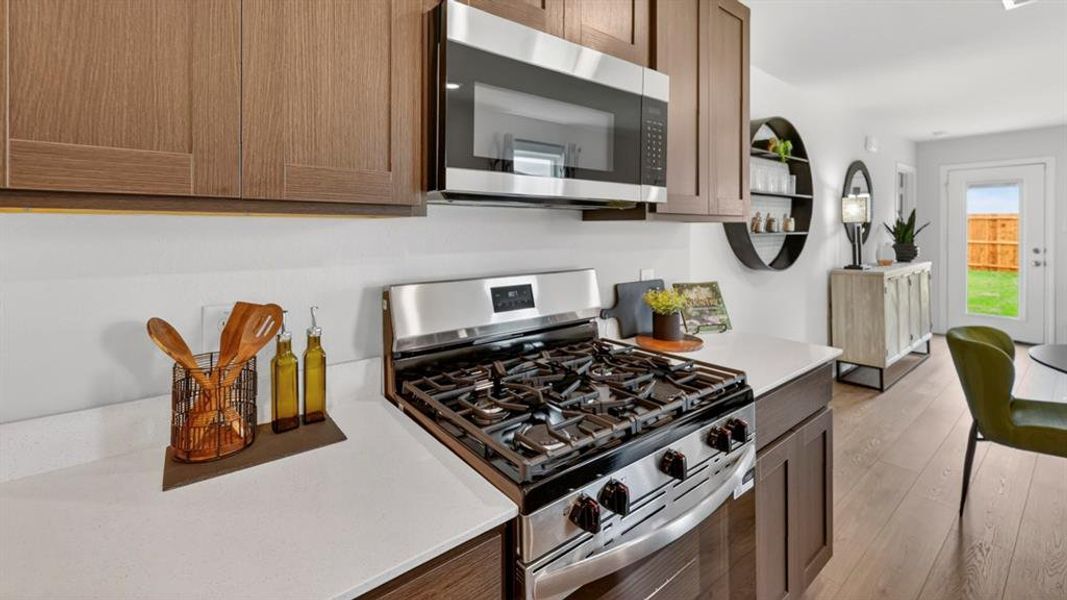 Modern kitchen featuring wood-finish cabinetry, stainless steel appliances, white countertops, and wood-finish flooring Modern kitchen featuring wood-finish cabinetry, stainless steel appliances, white countertops, and wood-finish flooring