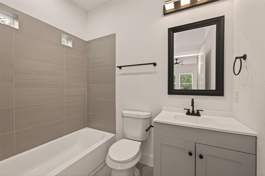 This bathroom features a sleek design with neutral tones. It includes a bathtub with modern tile surround, a vanity with a black-framed mirror, and stylish fixtures, creating a clean and inviting space. This bathroom features a sleek design with neutral tones. It includes a bathtub with modern tile surround, a vanity with a black-framed mirror, and stylish fixtures, creating a clean and inviting space.