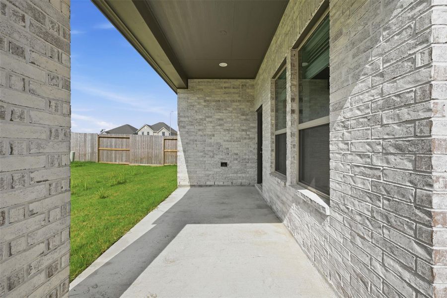 Spacious covered patio with brick detailing, perfect for outdoor relaxation and overlooking a lush green lawn.