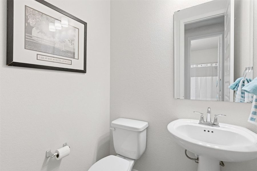 Pedestal sink with chrome faucet, a white toilet, and a wall-mounted mirror