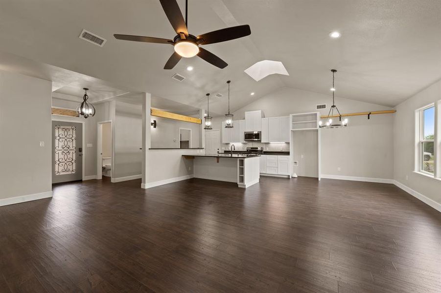 Unfurnished living room with a chandelier, vaulted ceiling, a ceiling fan, recessed lighting, and dark wood-style flooring