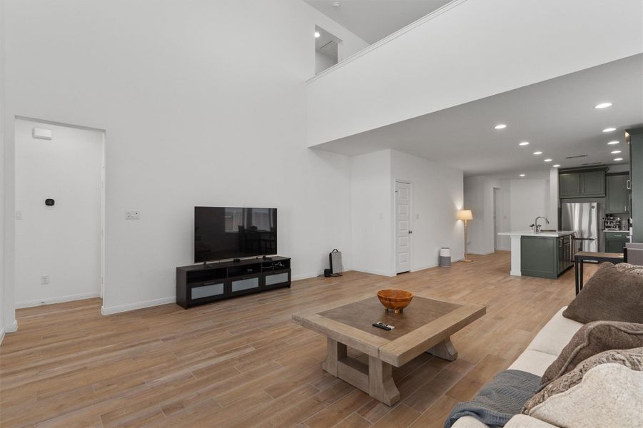 Living room with recessed lighting, light wood-style flooring, and a high ceiling