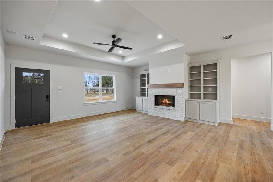 Unfurnished living room featuring ceiling fan, a fireplace, a raised ceiling, and light wood-type flooring