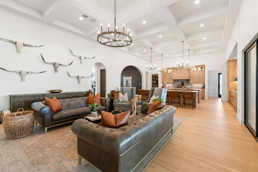 Living area featuring arched walkways, a chandelier, a high ceiling, coffered ceiling, and light wood-style floors Living area featuring arched walkways, a chandelier, a high ceiling, coffered ceiling, and light wood-style floors