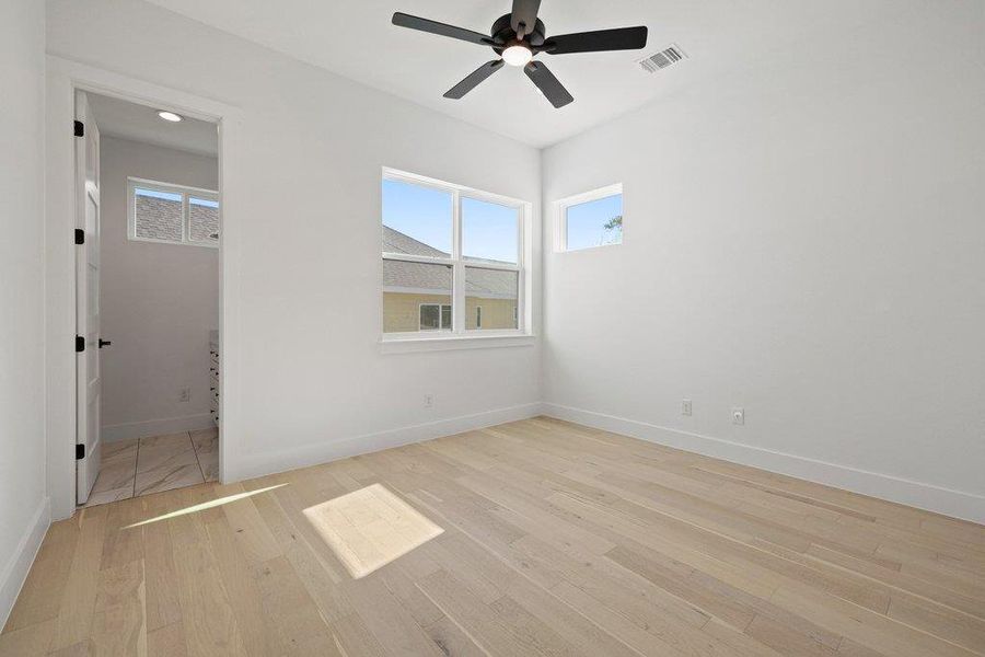 Unfurnished bedroom featuring light wood-type flooring, ceiling fan, multiple windows, and ensuite bathroom