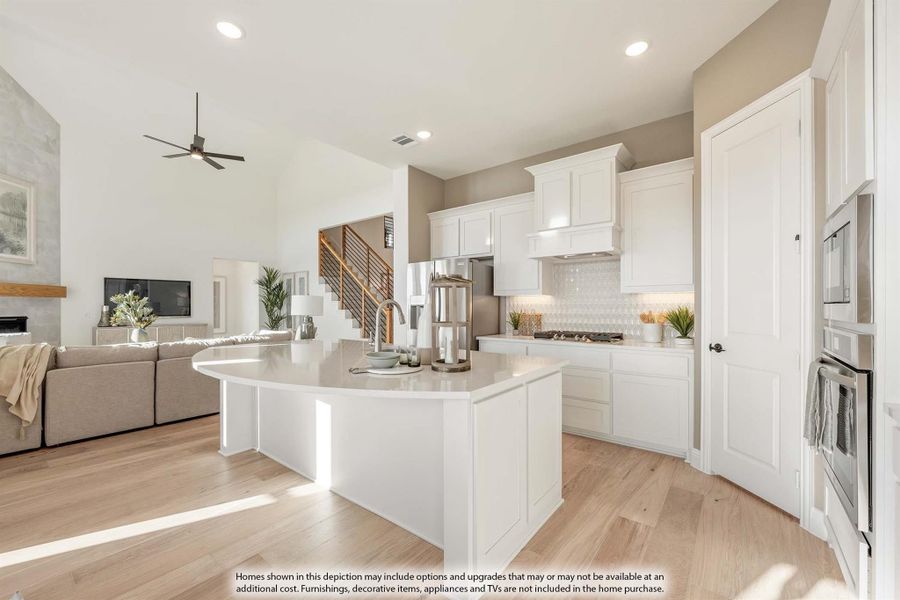 Open-concept kitchen with curved white island, white cabinets, and light wood floors open to living room Open-concept kitchen with curved white island, white cabinets, and light wood floors open to living room
