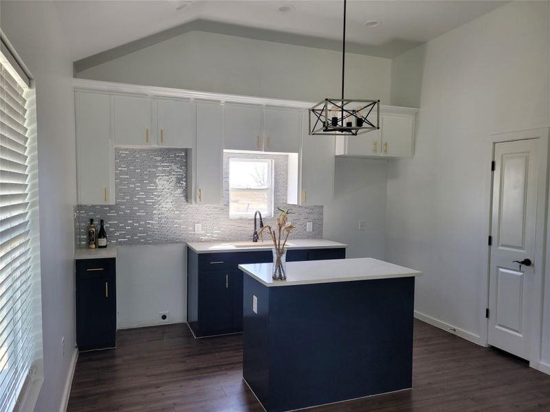 Kitchen with a kitchen island, pendant lighting, dual tone cabinetry, tasteful backsplash, and dark wood-type flooring