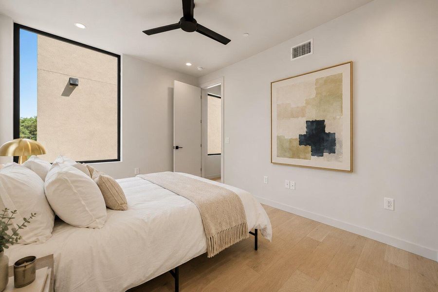 Natural light illuminates a cozy bedroom featuring sleek hardwood flooring and a contemporary ceiling fan. Natural light illuminates a cozy bedroom featuring sleek hardwood flooring and a contemporary ceiling fan.