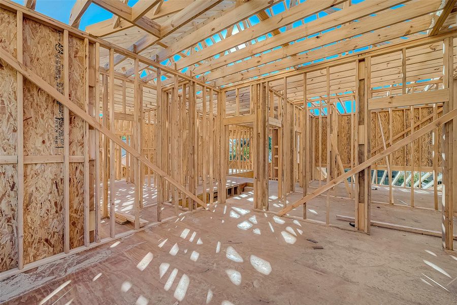 The photo shows the interior framing of a new construction home, featuring exposed wooden beams and studs. The structure is in an unfinished state, allowing for customization and layout planning.