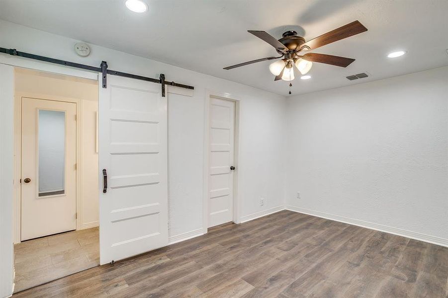 Unfurnished bedroom with recessed lighting, wood finished floors, ceiling fan, and a barn door