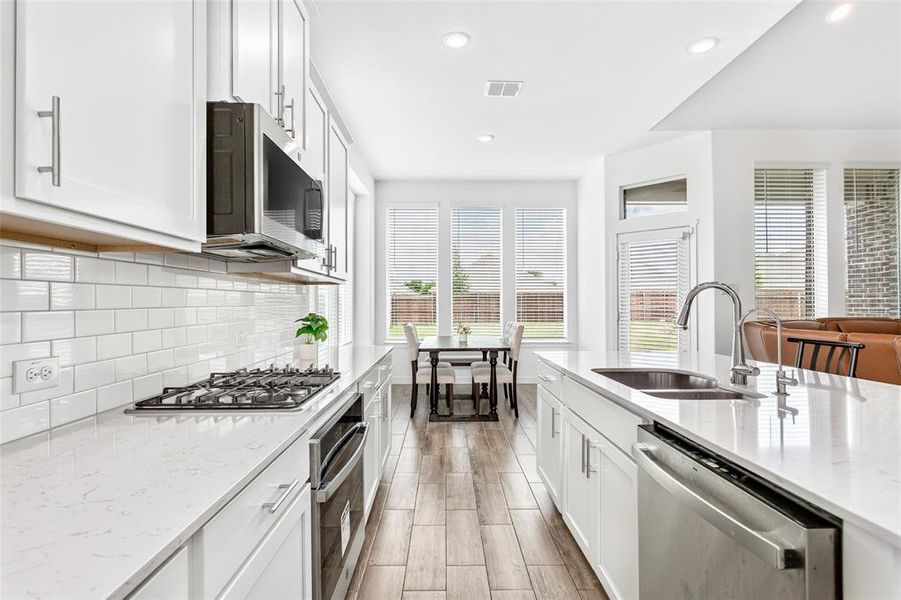 Kitchen featuring white cabinetry, subway tile backsplash, stainless steel appliances, wood-finish flooring, and white countertops