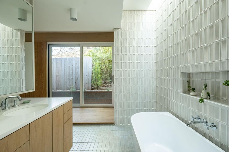 Bathroom featuring light tile patterned floors, vanity, a freestanding bath, and tile walls