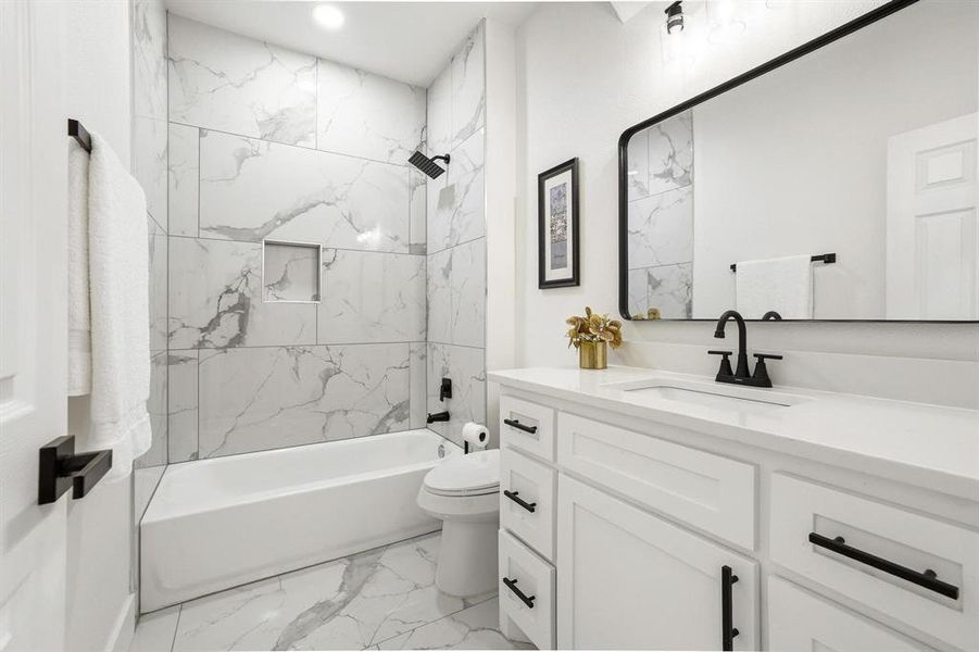 Modern downstairs bathroom with marble tile, tub/shower, and black fixtures. Modern downstairs bathroom with marble tile, tub/shower, and black fixtures.
