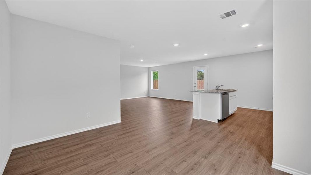 Open-concept living area featuring wood-finish flooring, recessed lighting, and a kitchen island with a built-in sink, dishwasher, and stone-look countertop