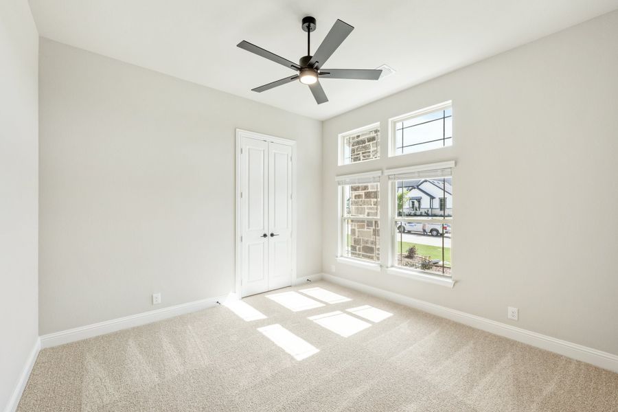 Empty bedroom with carpet flooring, ceiling fan, double doors, and large windows with neighborhood view Empty bedroom with carpet flooring, ceiling fan, double doors, and large windows with neighborhood view
