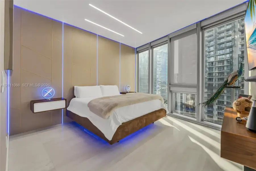 Floor-to-ceiling windows, custom paneled accent wall with integrated LED lighting, floating built-in bedside storage, and high-gloss tile flooring Floor-to-ceiling windows, custom paneled accent wall with integrated LED lighting, floating built-in bedside storage, and high-gloss tile flooring